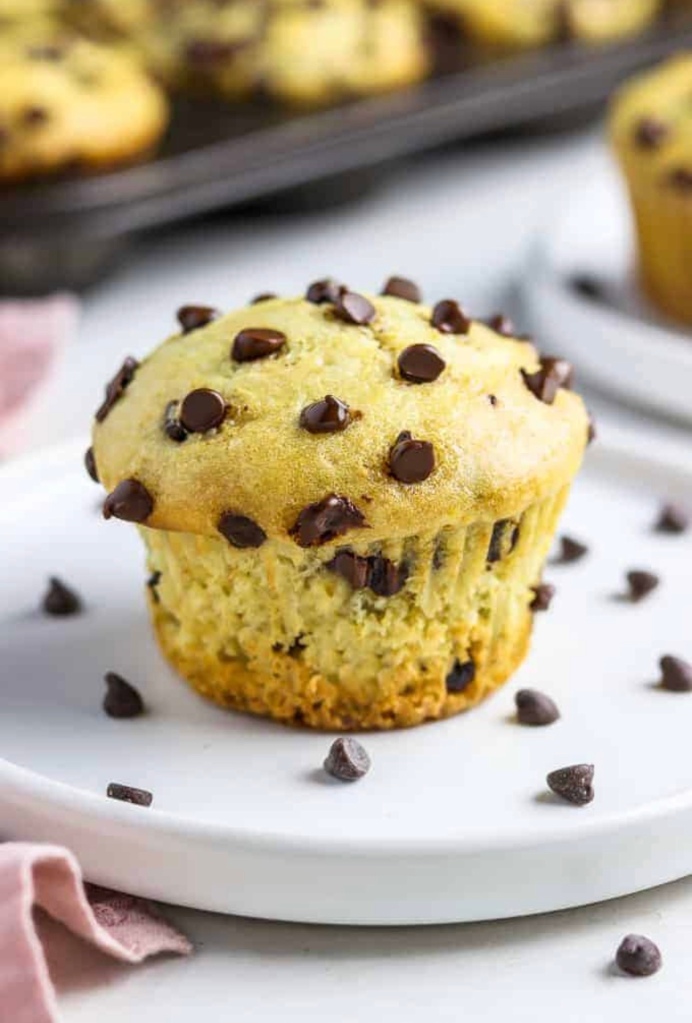 close up photo of vegan chocolate chip muffin on a white plate with more muffins in the background. 